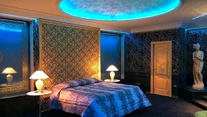 Ein Schlafzimmer mit einem Bett, zwei Nachttischlampen, einer runden Deckenleuchte, strukturierten Tapeten und einer Statue.
