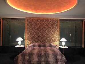 A hotel room with a large bed, two bedside lamps, a patterned headboard, and a circular ceiling light.