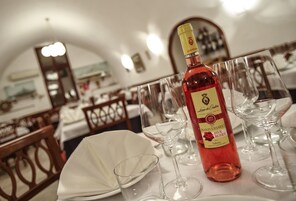 Egy étkezőasztal, melyen borospoharak és egy borosüveg található, egy olyan szobában, melynek berendezése fából készült, és az asztalt fehér terítő borítja.