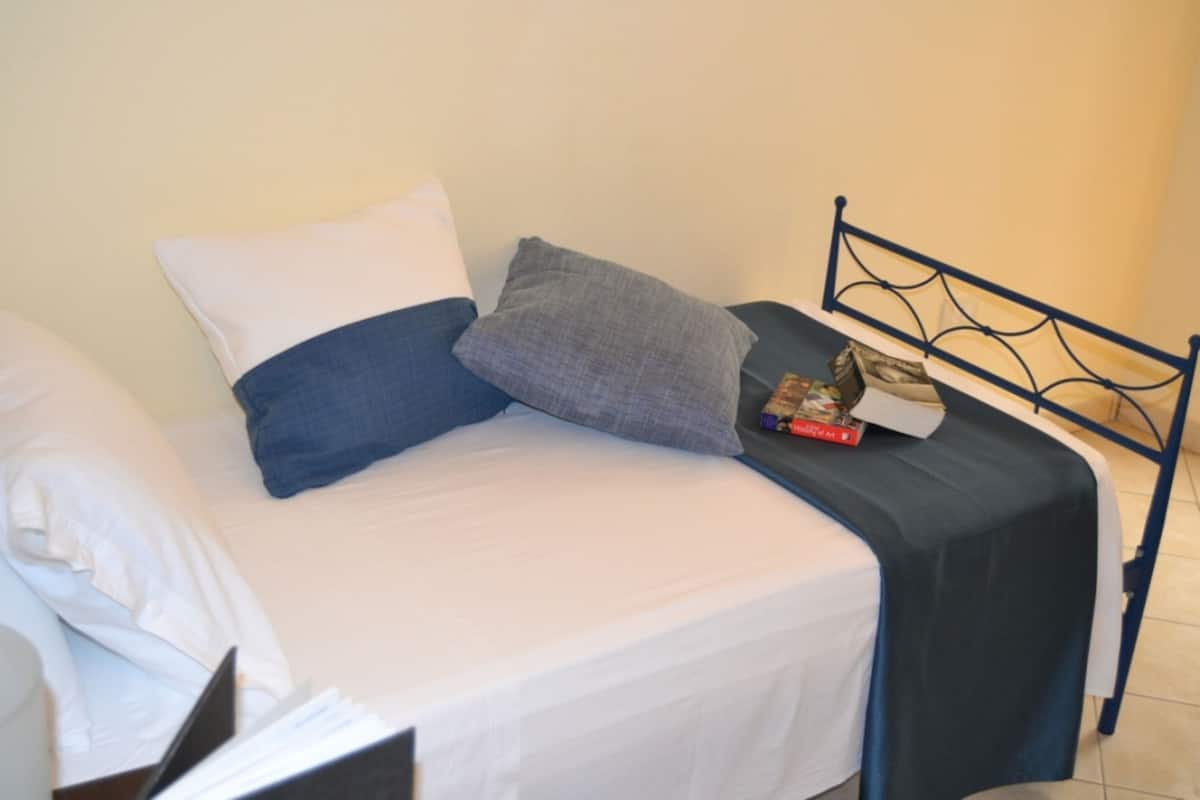 A bed with white and blue bedding, a metal headboard, and a book on the side.