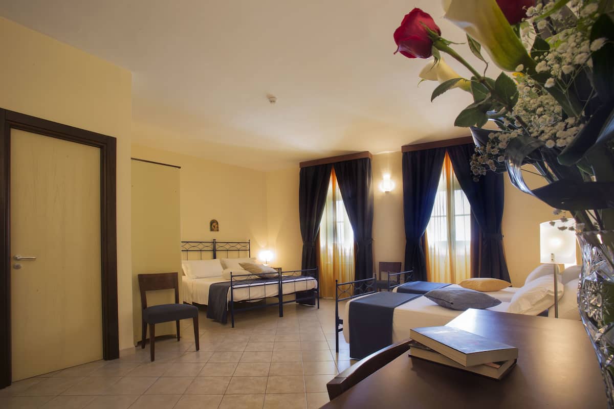 A hotel room with a bed, a desk, a chair, and a vase with flowers.