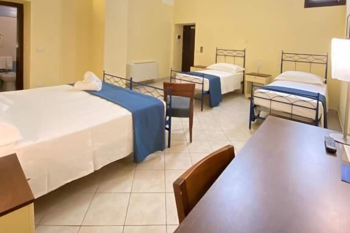 A hotel room with three beds, a wooden desk, and a chair.