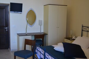 Un dormitorio con cama, escritorio, silla, armario, espejo y televisor en la pared.