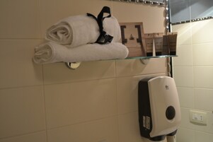 Un baño con un estante de vidrio que sostiene una toalla enrollada y artículos de tocador.