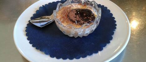 A dessert in a glass bowl on a white plate with a blue scalloped edge, placed on a metal surface.