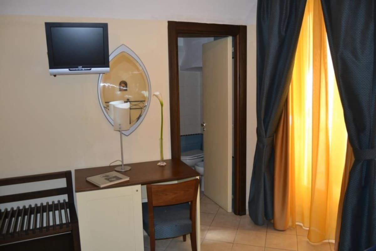 A hotel room with a desk, chair, television, mirror, and a view of the bathroom.