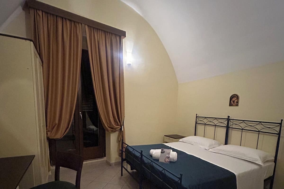 A bedroom with a bed, a chair, a nightstand, and a window with curtains.