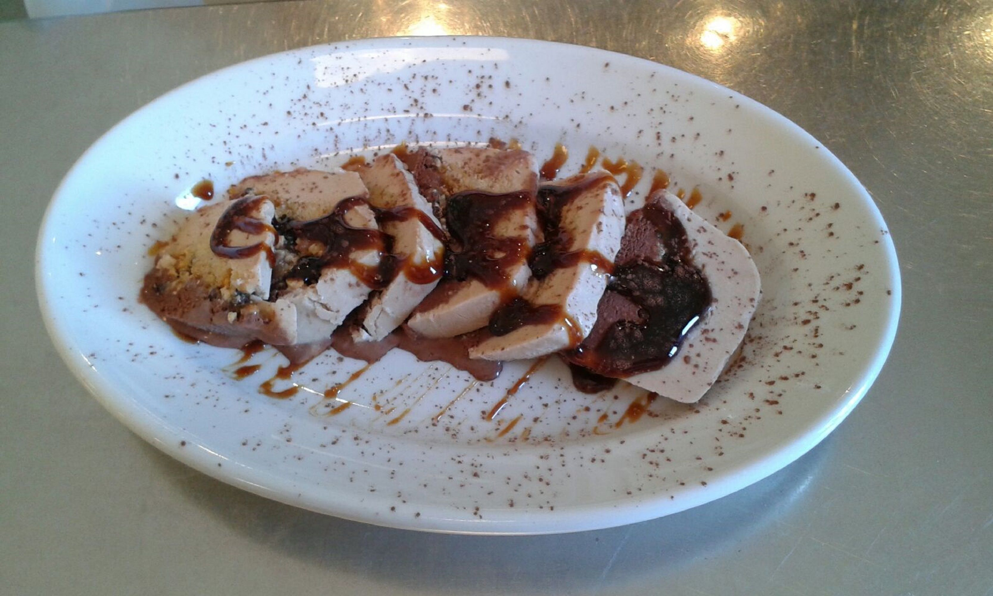 A white plate with sliced meat and sauce on a metal surface.