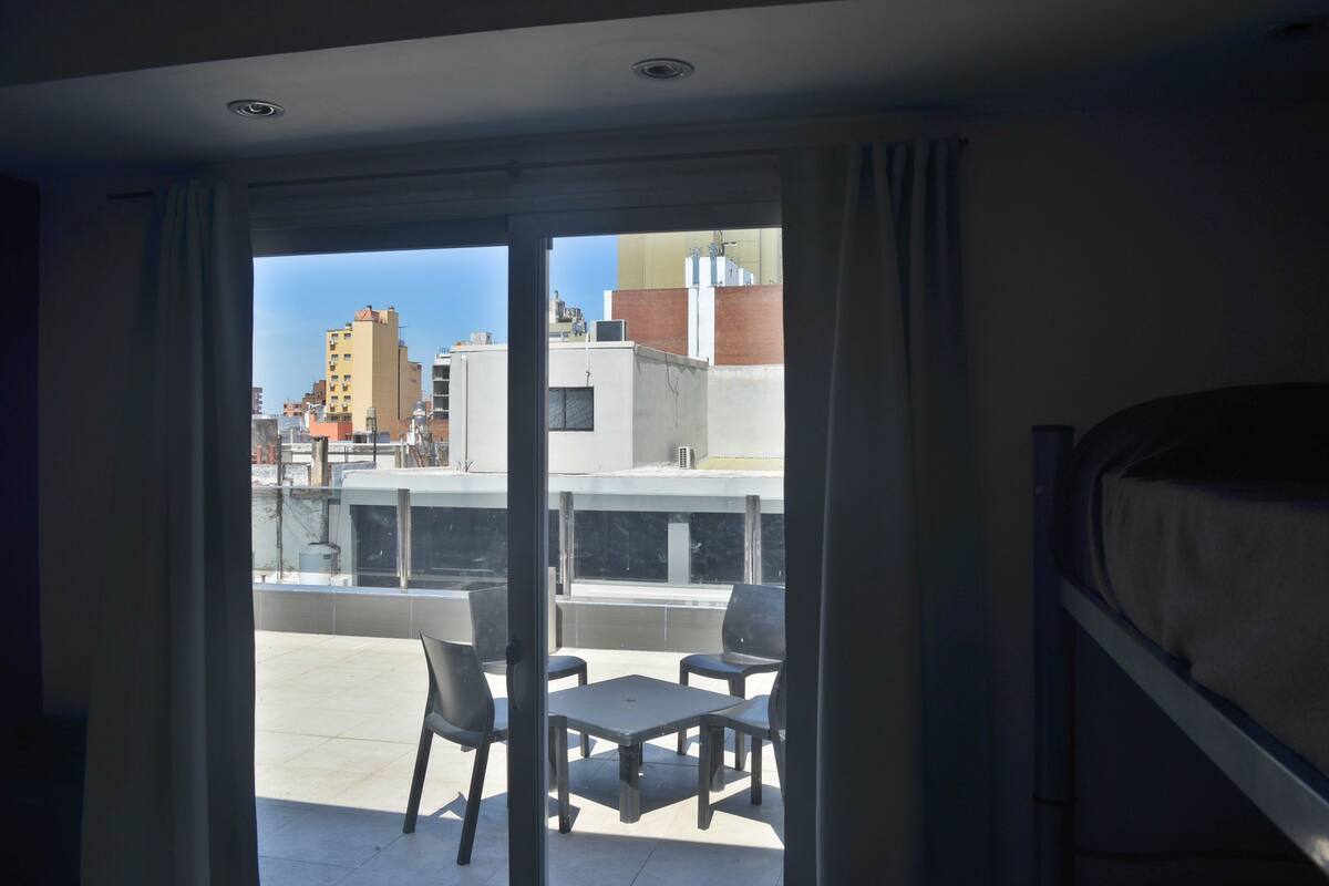 A room with a balcony, a bed, and a view of buildings.
