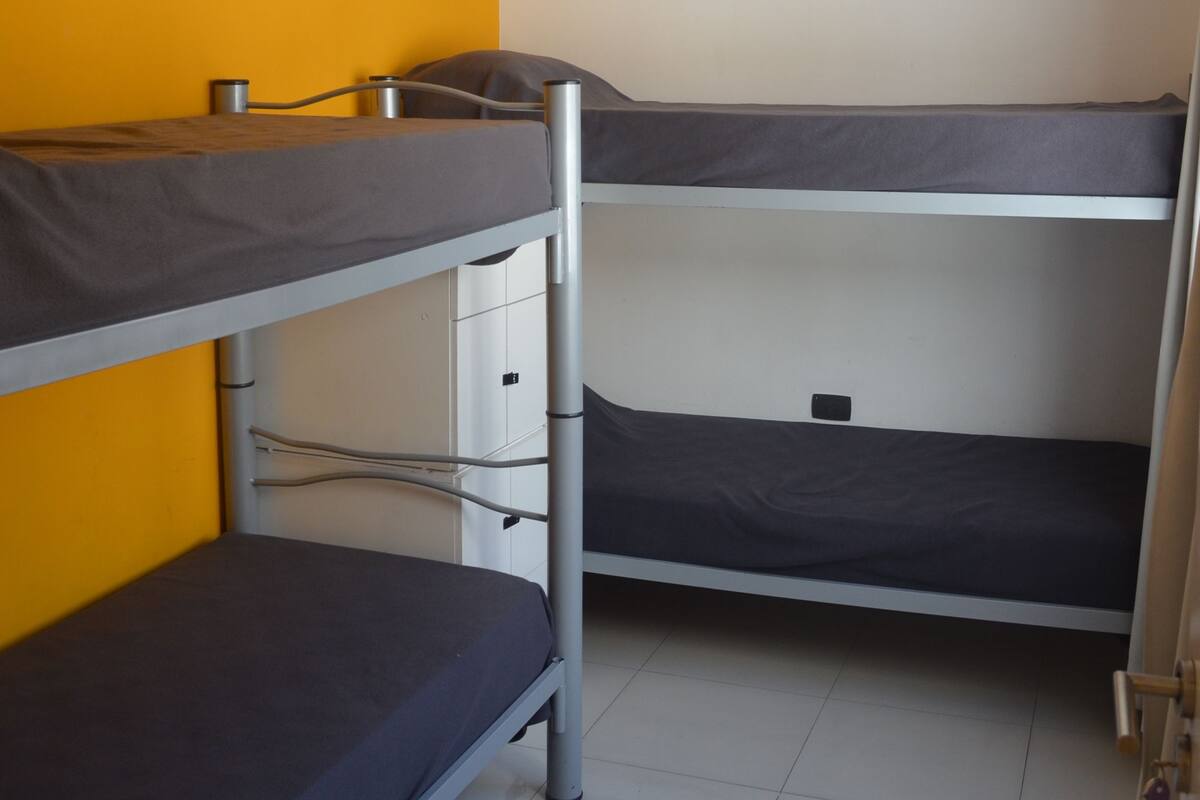 A bunk bed room with a ceiling fan, white walls, and a yellow accent wall.