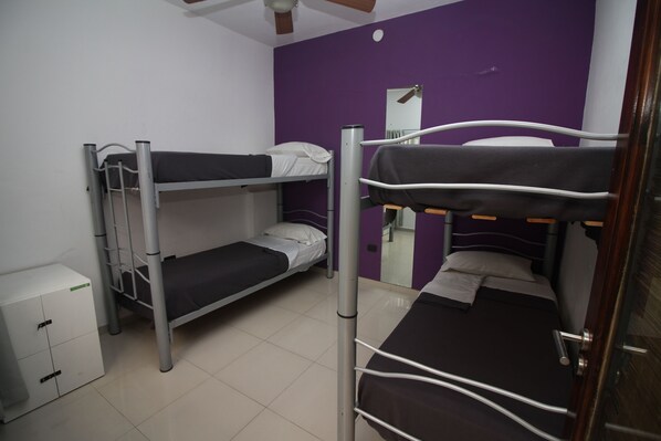 Un dormitorio con literas, un armario pequeño y un ventilador de techo.