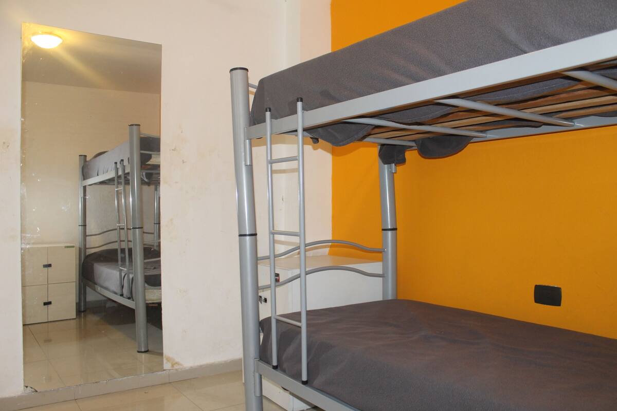 A bunk bed room with a metal frame, a grey mattress, and an orange wall.