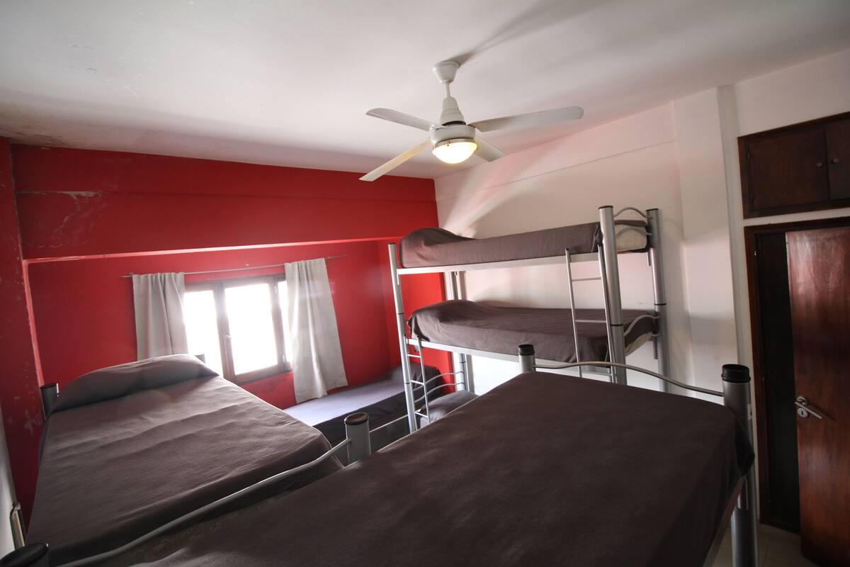 A dormitory room with bunk beds, a ceiling fan, and a window with curtains.