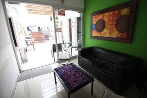A room with a black leather sofa, a patterned ottoman, and a colorful abstract painting on a green wall. - Link Cordoba Hostel (Córdoba)