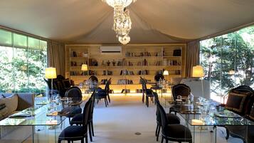 Una habitación lujosa con una gran araña, una mesa de comedor de cristal rodeada de sillas y una estantería llena de libros.