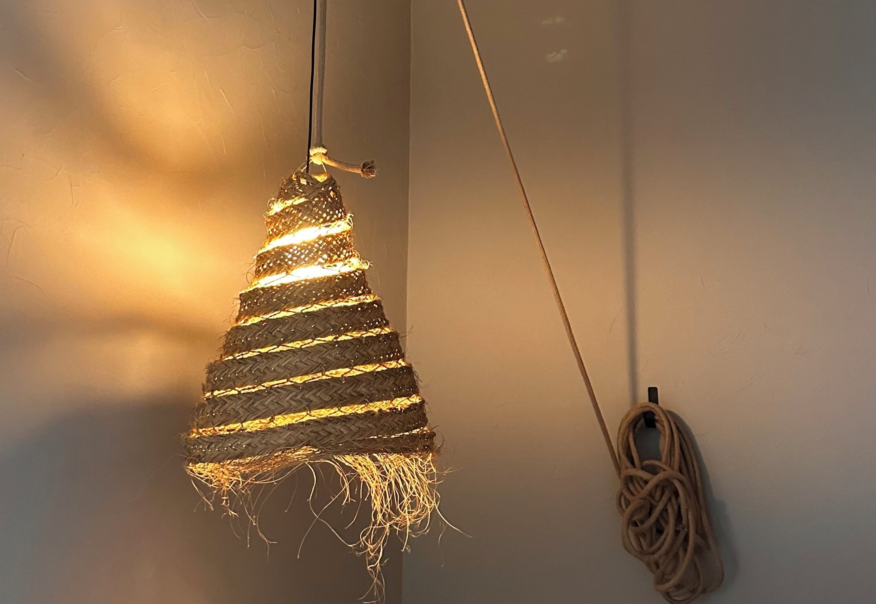 Eine Pendelleuchte mit gewebtem Design und einem umwickelten Kabel an der Wand.