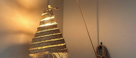 A hanging light fixture with a woven design and a coiled cable on the wall.