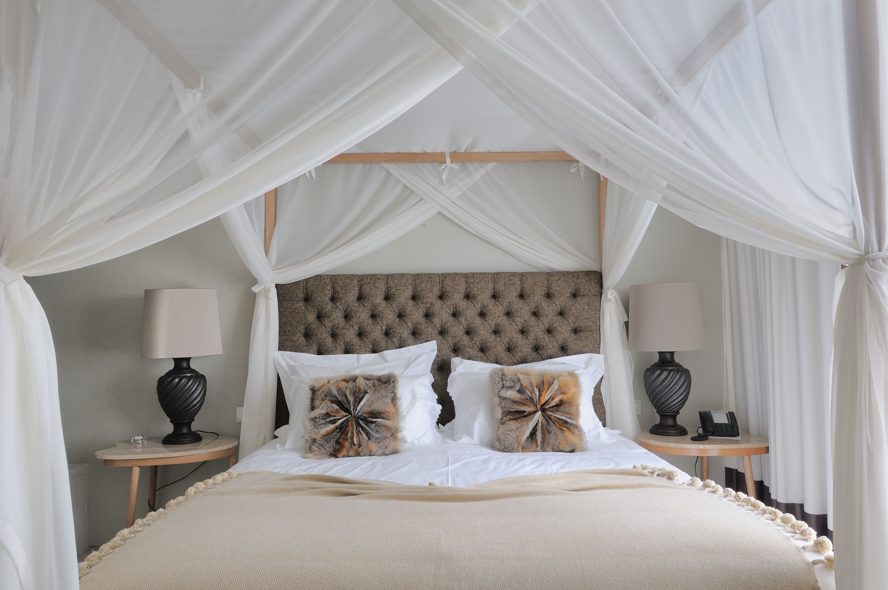 A bed with a canopy, two bedside tables with lamps, and a tufted headboard.