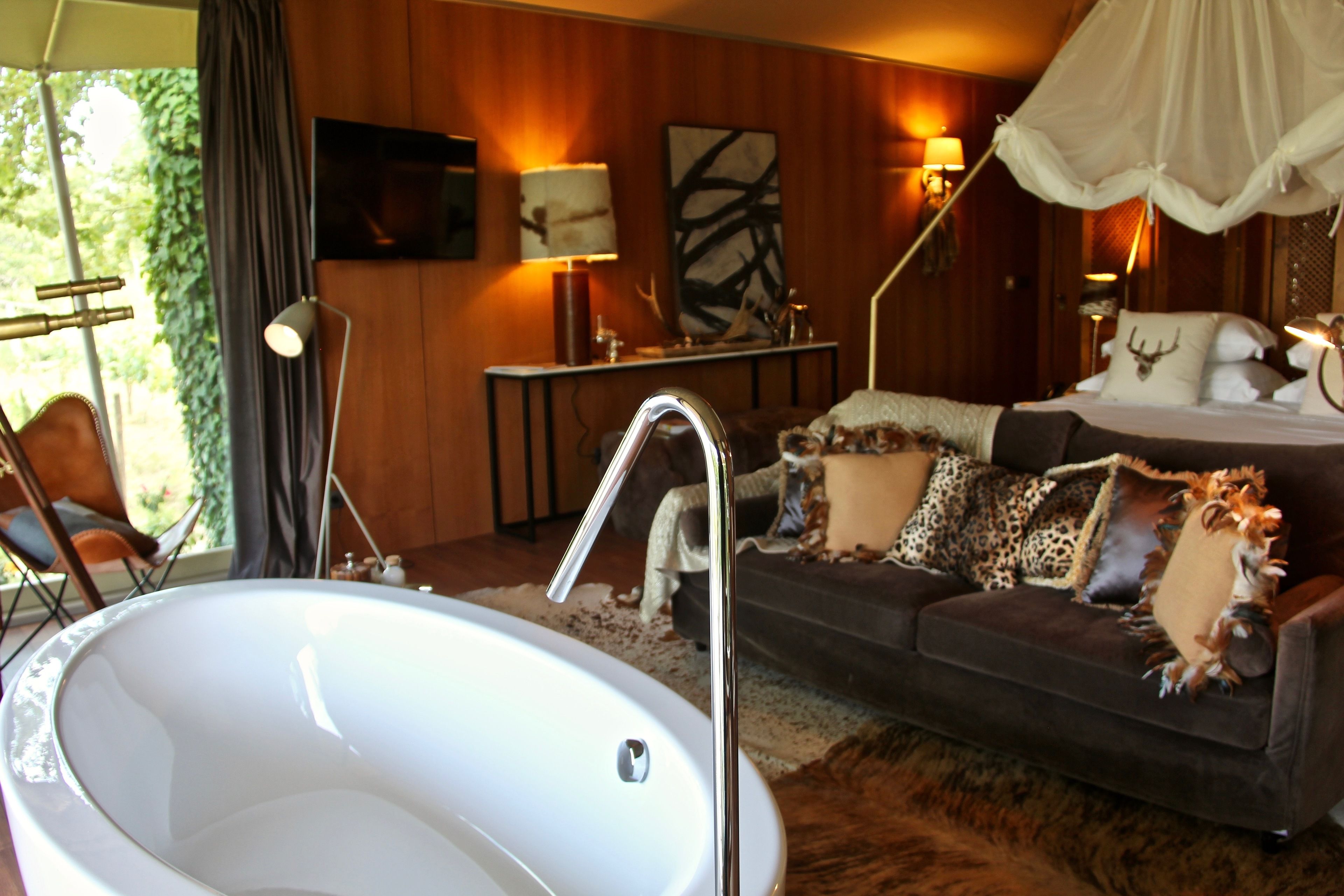 A room with a large white bathtub, a dark brown sofa with patterned cushions, and a canopy bed with a deer head pillow.