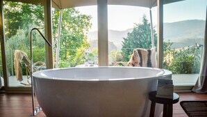 Une grande baignoire sur pieds, placée dans une pièce dotée de grandes fenêtres donnant sur un paysage montagneux.