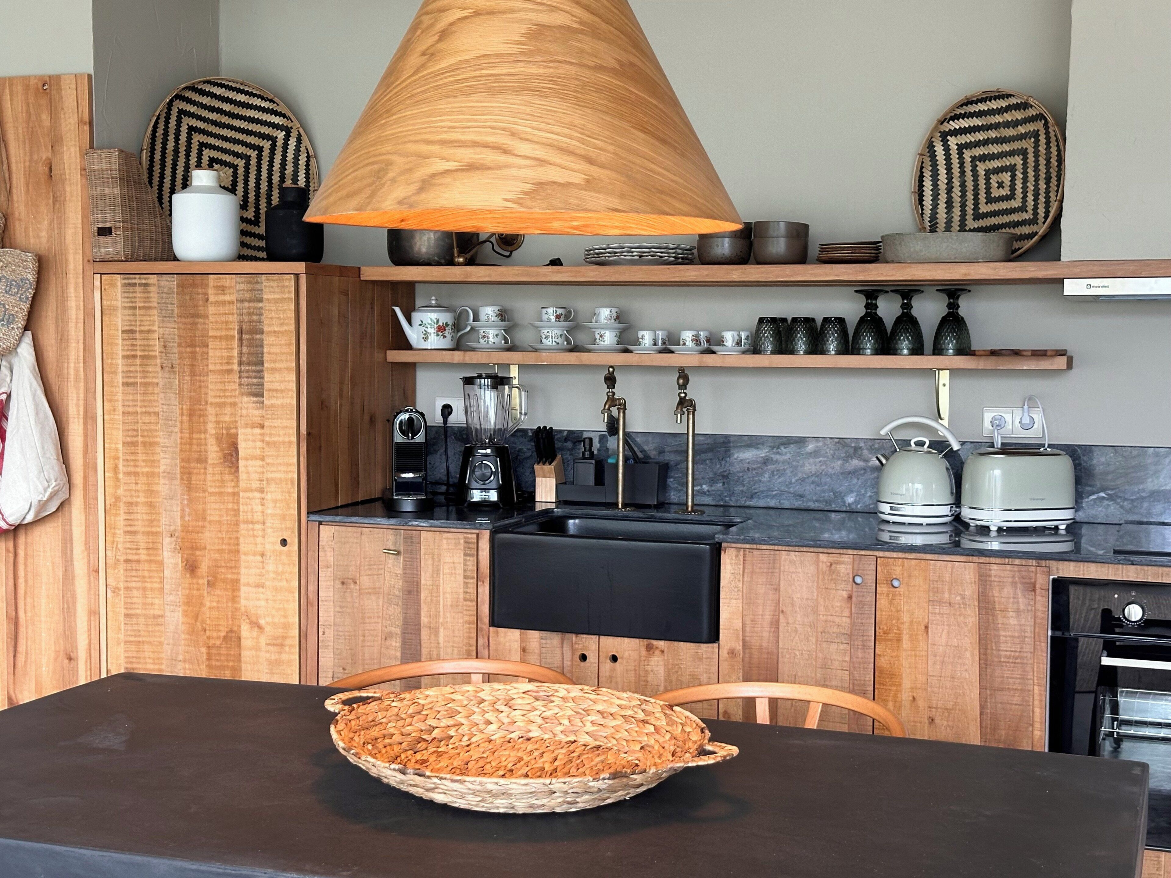 Una cocina con armarios de madera, encimera negra, una cesta tejida, cafetera, hervidor y tostadora.