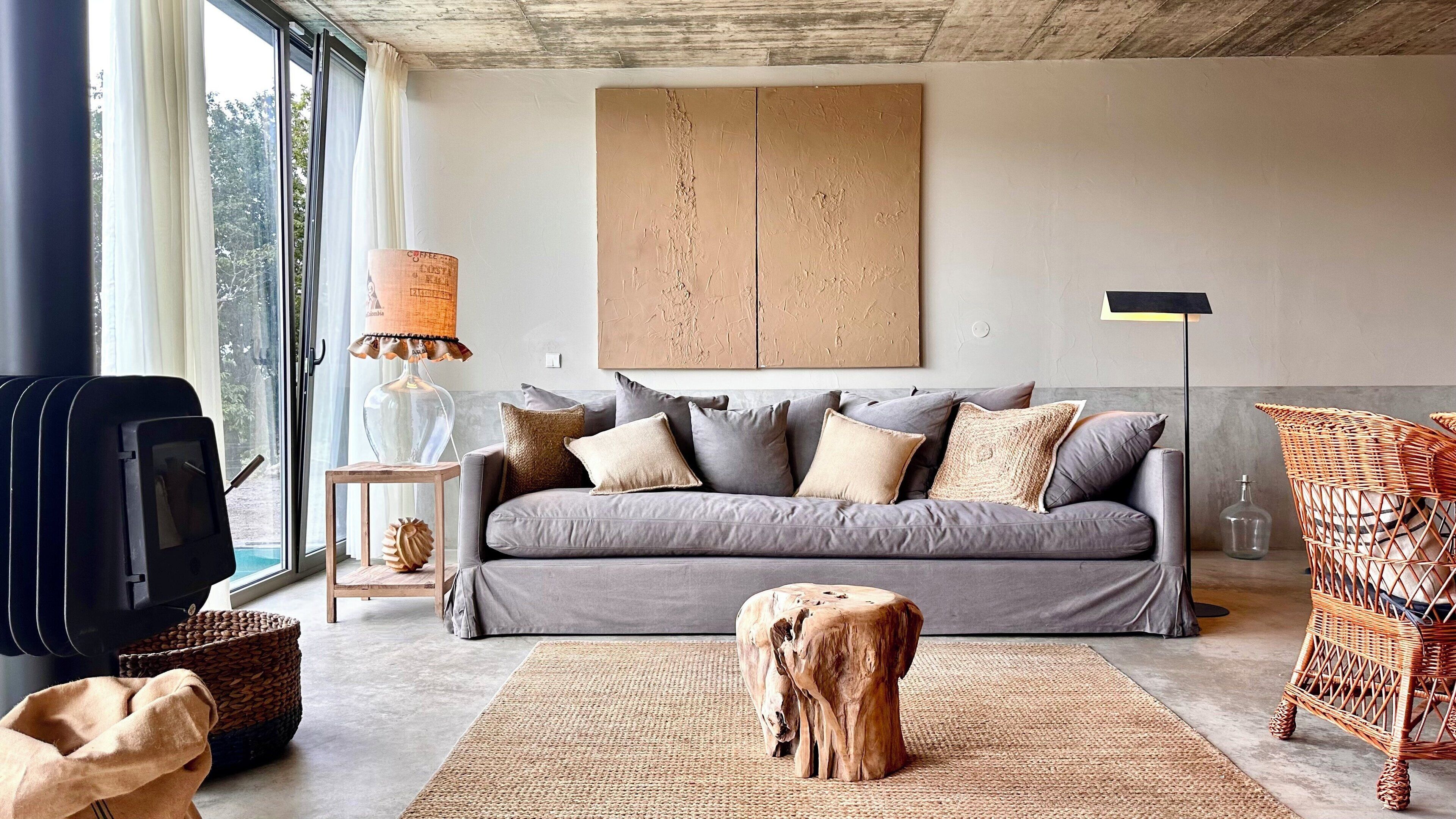 A modern living room with a grey sofa, a coffee table, a wooden stool, a wicker chair, a floor lamp, and a large abstract painting on the wall.