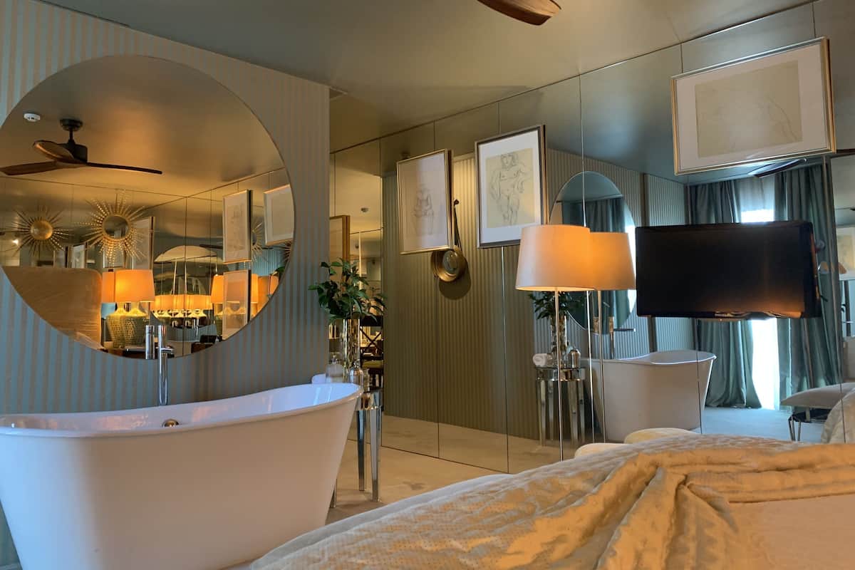 Habitación de hotel moderna con un espejo grande, una bañera, un televisor de pantalla plana y un ventilador de techo.