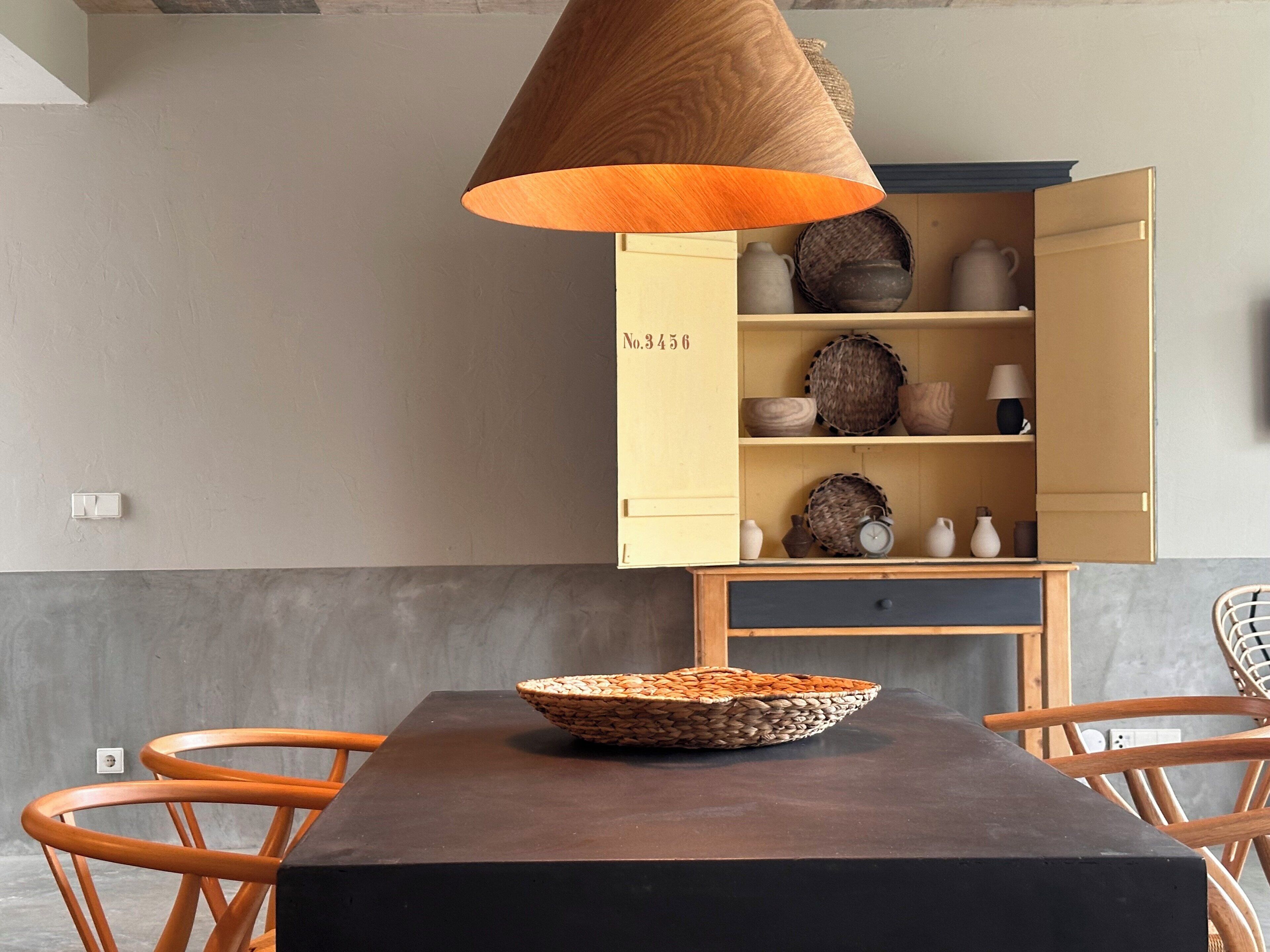 A dining area with a table, chairs, a basket, a cabinet with shelves, and a hanging lamp.