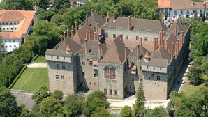 Un grand bâtiment historique en pierre, doté de nombreuses tours et tourelles, et entouré d’une végétation luxuriante.