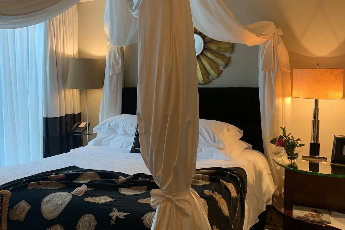 Una habitación de hotel con una cama con dosel, una mesita de noche con lámpara y un reloj de pared.