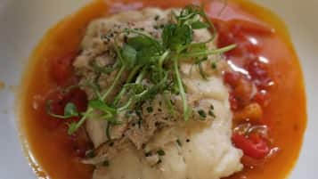A white plate with a fish fillet topped with greens and sauce.