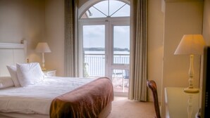 A hotel room with a large bed, a view through a glass door, and a chair by the window. - WatersEdge Hotel (Cobh)