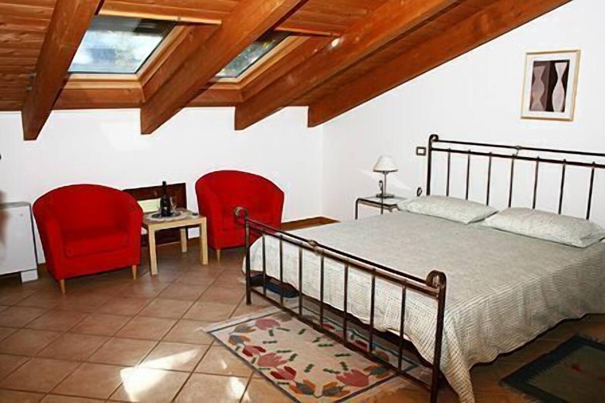 A bedroom with a bed, two red chairs, a small table, a lamp, and a skylight.