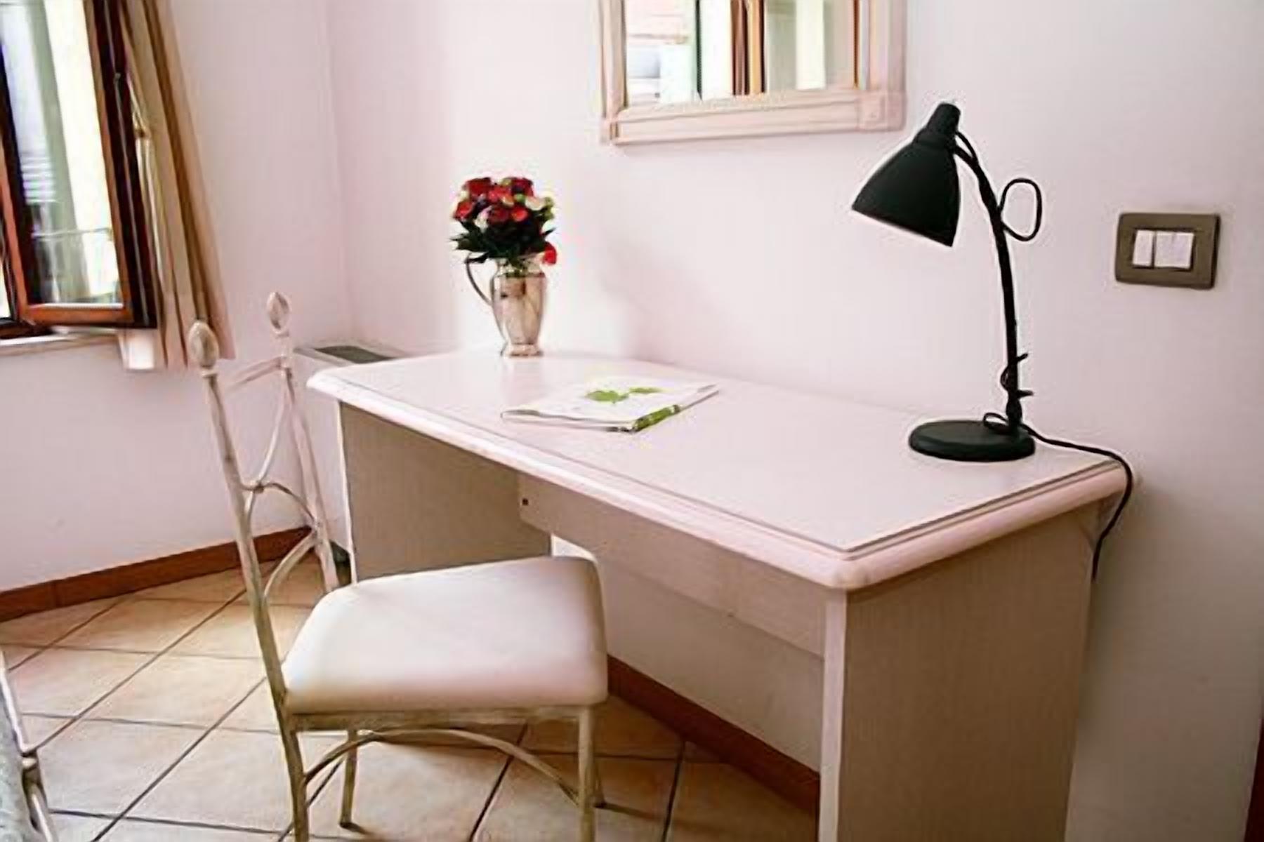 A small, white desk with a chair, a vase with flowers, and a desk lamp.