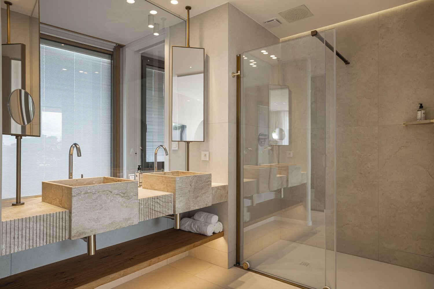 Een moderne badkamer met twee wastafels, een glazen douchecabine en een houten bankje.
