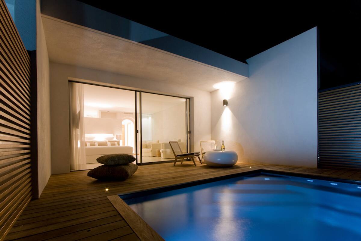 A modern outdoor pool area with a wooden deck, a lounge chair, and a seating area with cushions.