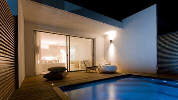 Un área de piscina exterior moderna con cubierta de madera, una tumbona y un espacio de estar con cojines.