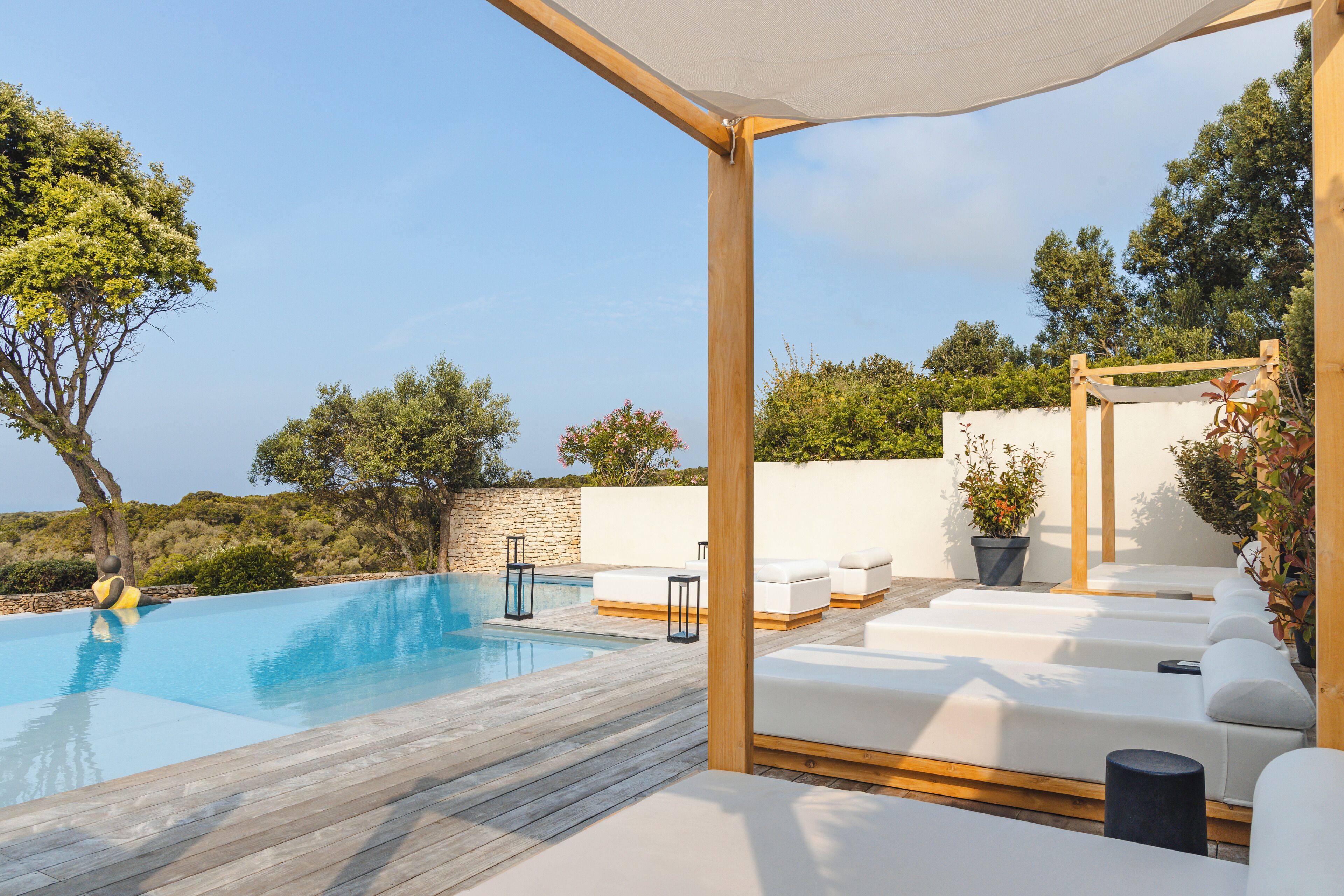 An outdoor swimming pool with wooden decking, white lounge chairs, and potted plants.