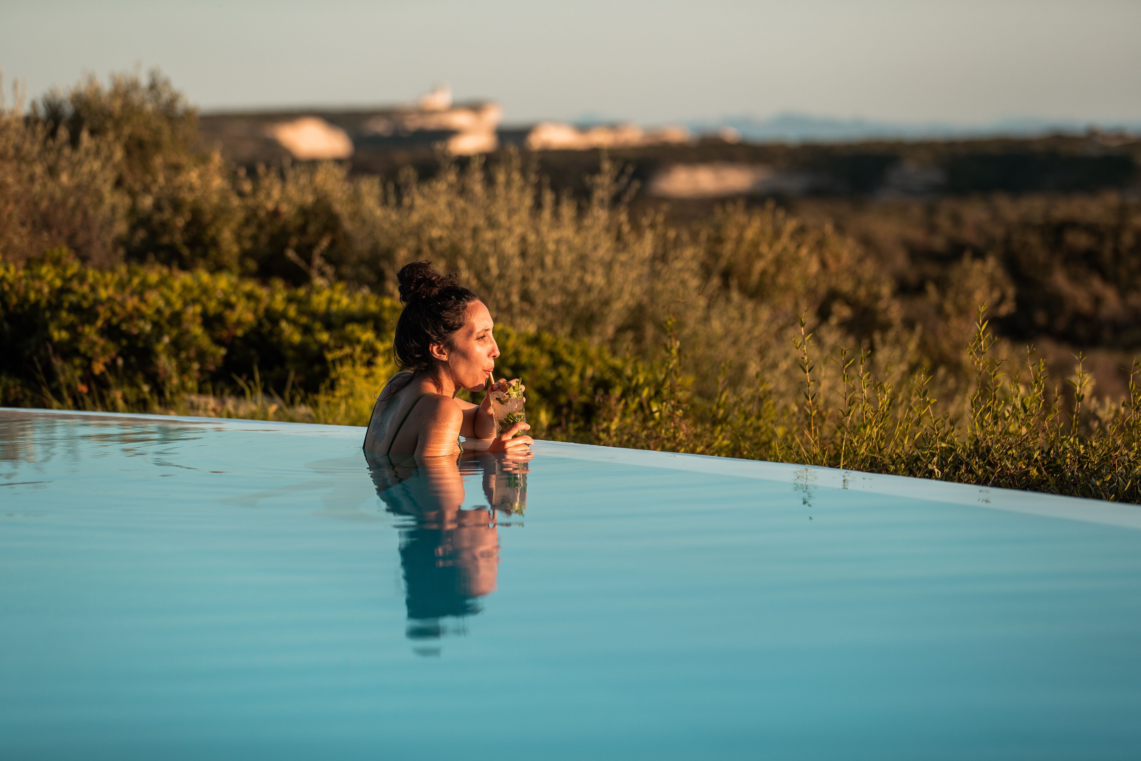 A person relaxing in a clear blue infinity pool with a view of a natural landscape in the background.
