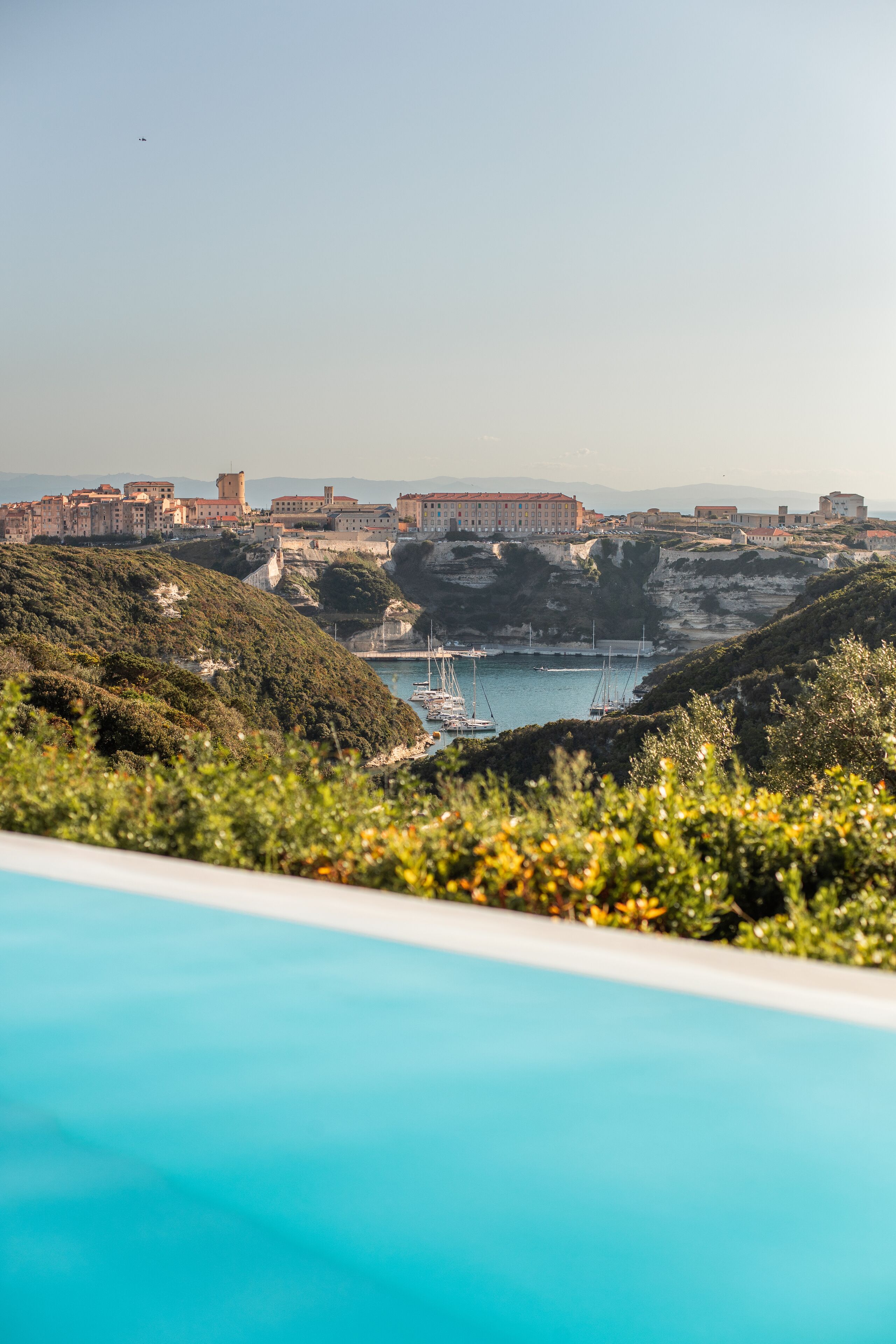 Vista costera con piscina, barcos y edificios en una colina.