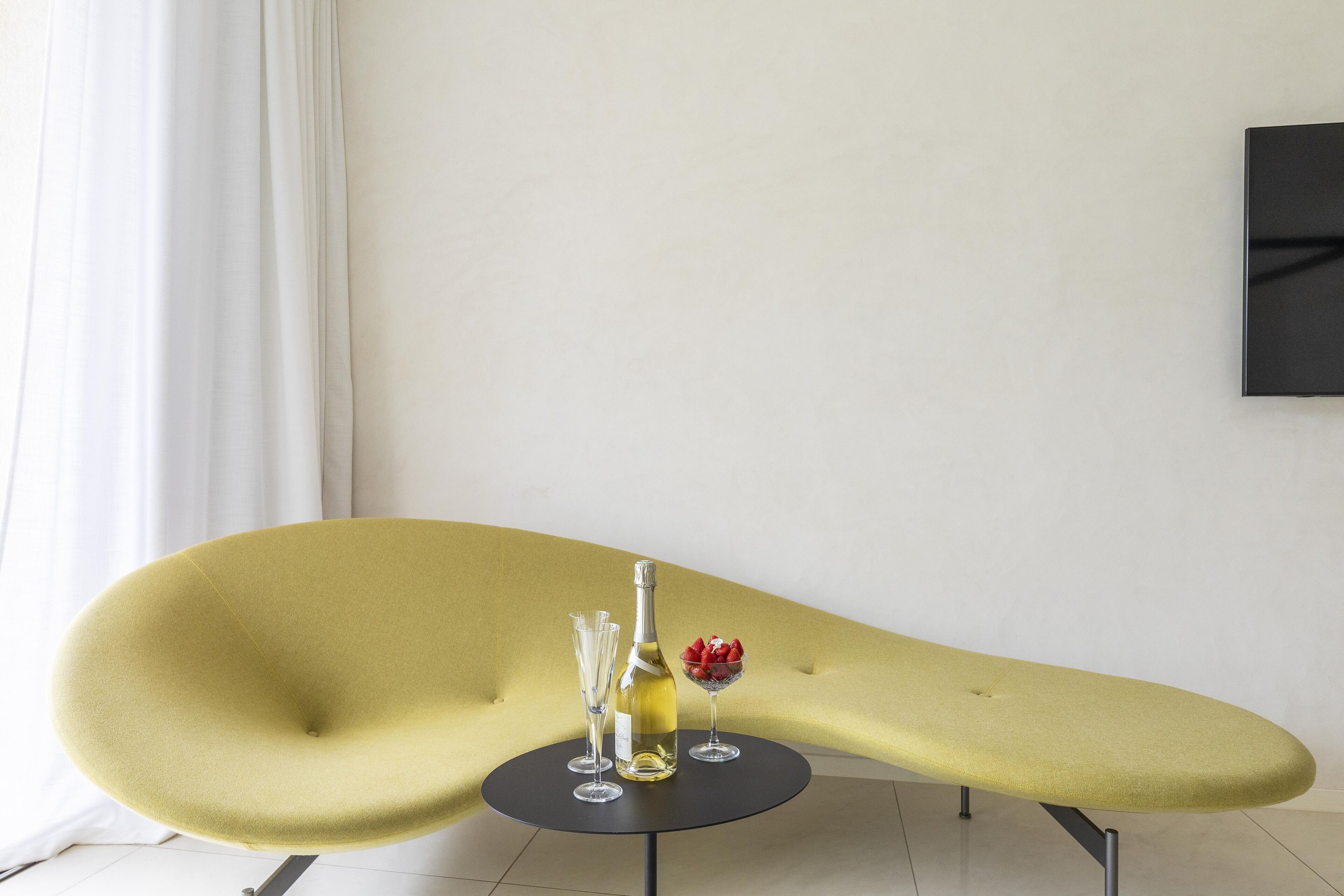 Un fauteuil jaune, une table ronde devant, une bouteille et un verre de vin rouge.