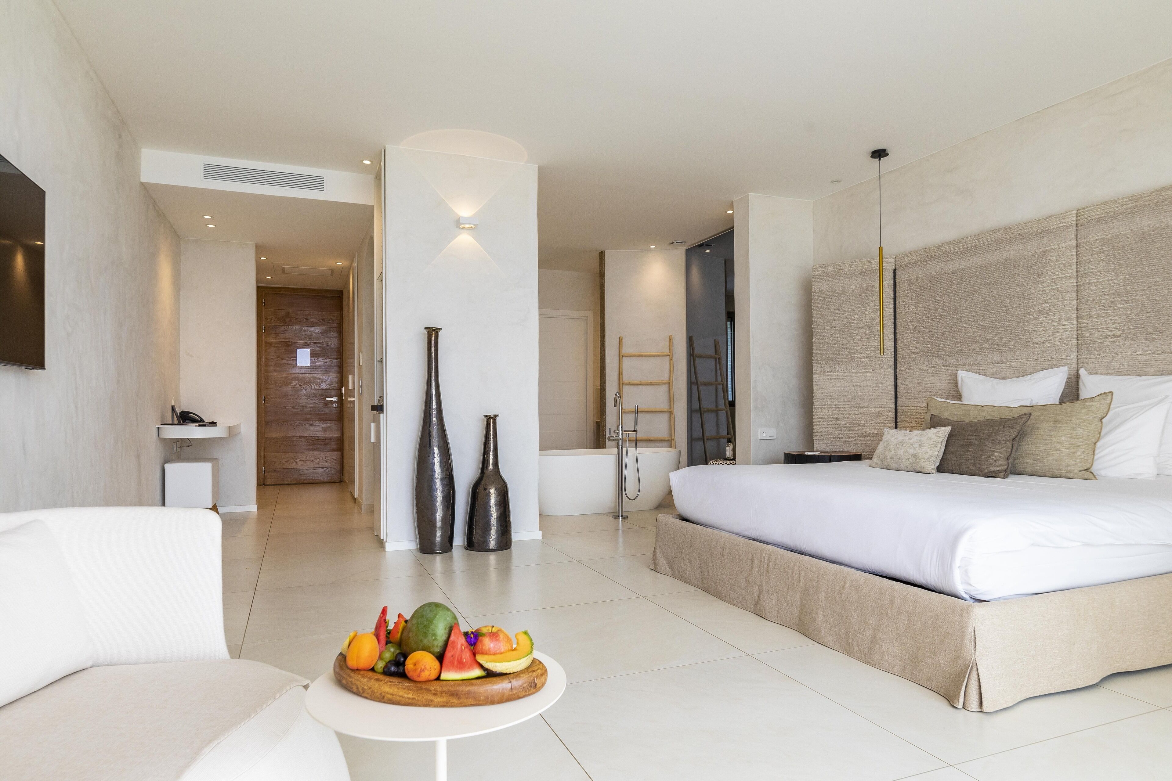 A modern hotel room with a large bed, a sofa, a fruit bowl, and a small table.