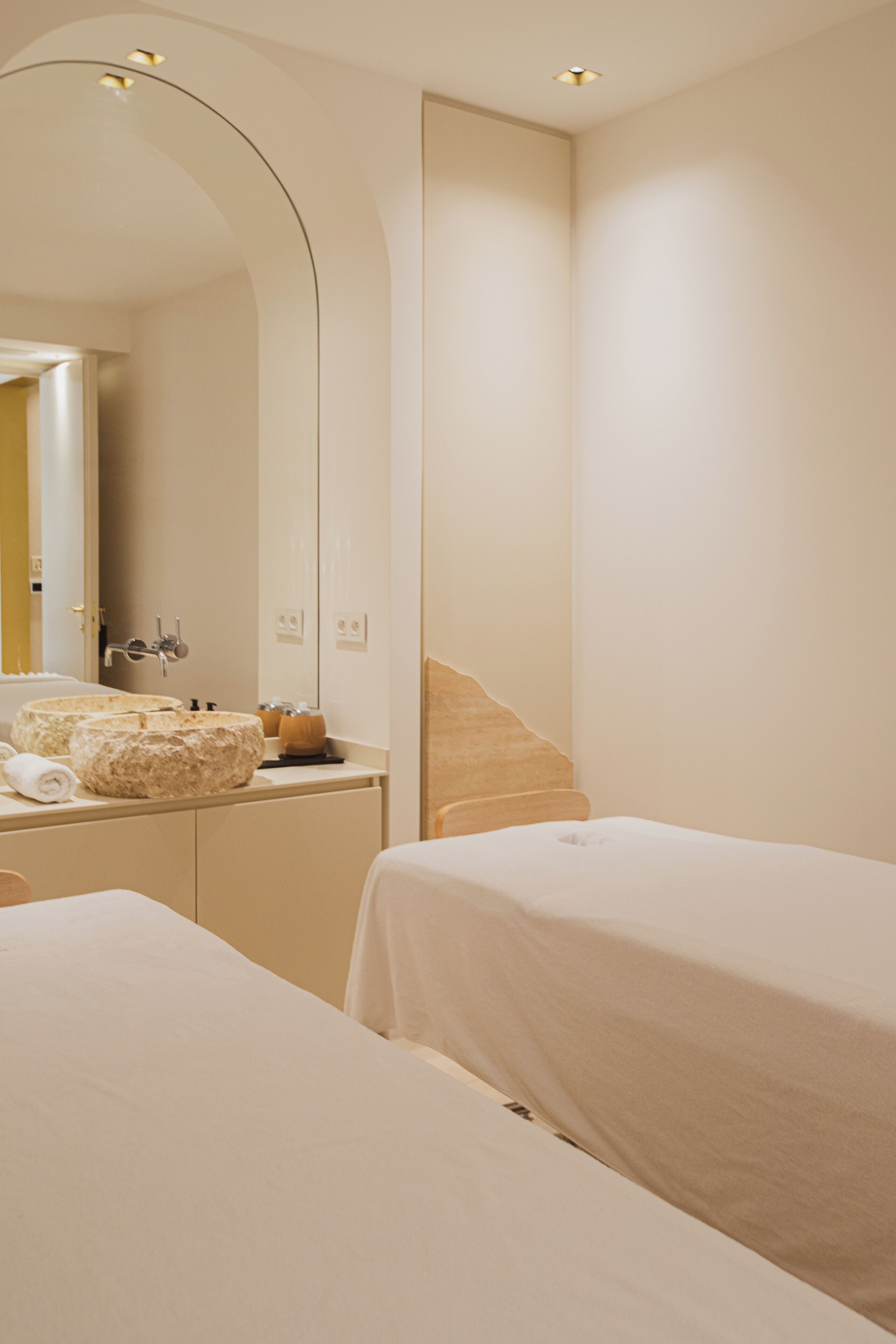 A hotel room with a large mirror, a bed, a bedside table, and a bathroom with a sink and mirror.
