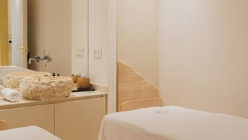 A hotel room with a large mirror, a bed, a bedside table, and a bathroom with a sink and mirror.