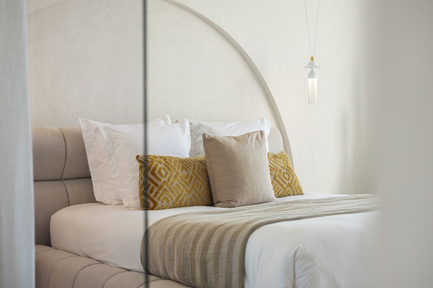 Ein modernes Schlafzimmer mit einem gewölbten Kopfteil, einem Bett mit weißen und gemusterten Kissen sowie einer hängenden Leuchte.