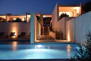 Un área de piscina moderna con una escalera que lleva a una terraza cubierta, rodeada de sillones de descanso y una cascada.