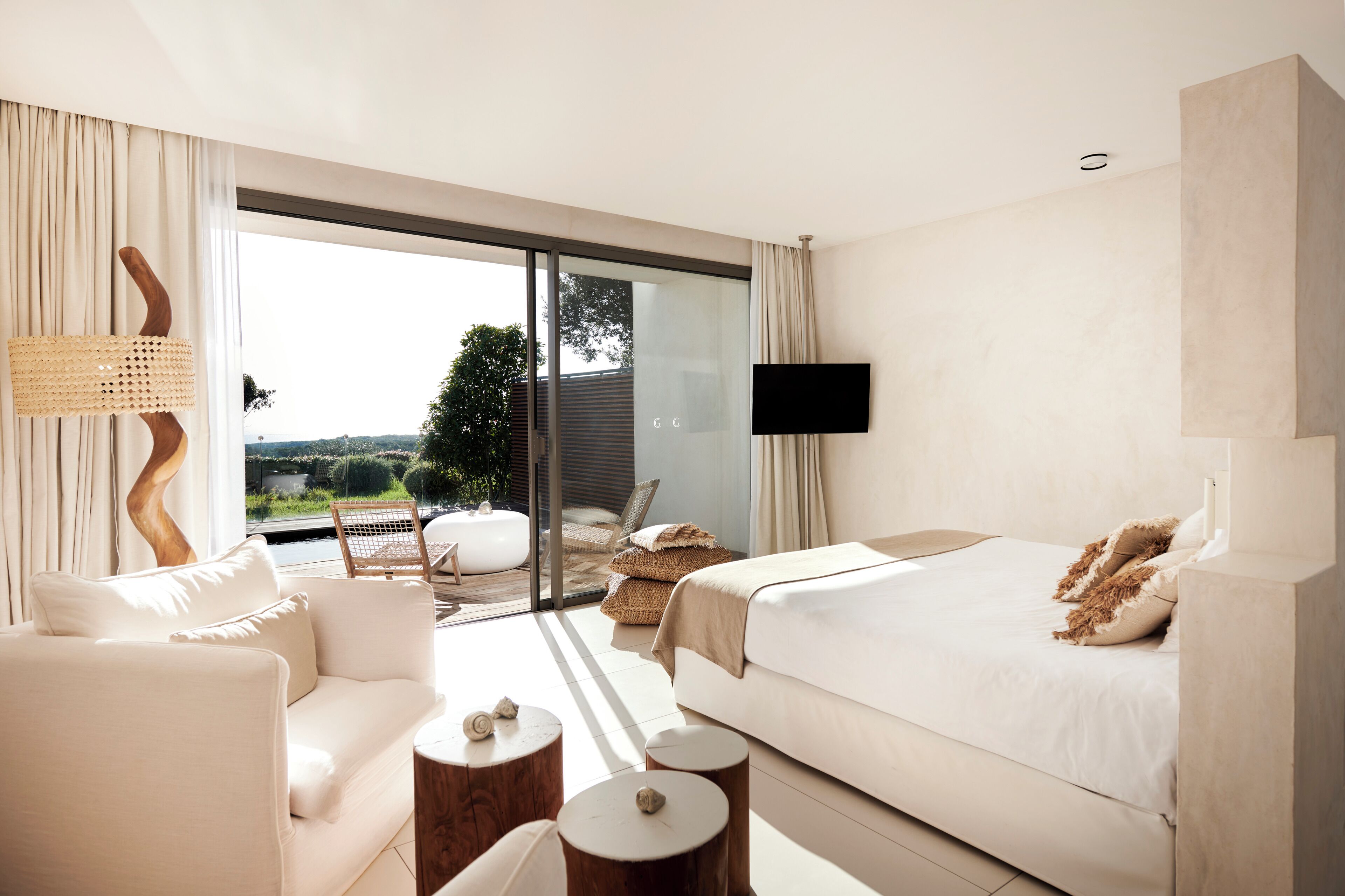 Habitación de hotel moderna con una cama grande, un sofá, un televisor y un balcón con mobiliario exterior.