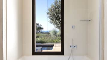 A modern bathroom with a large bathtub and a window overlooking a pool and greenery.