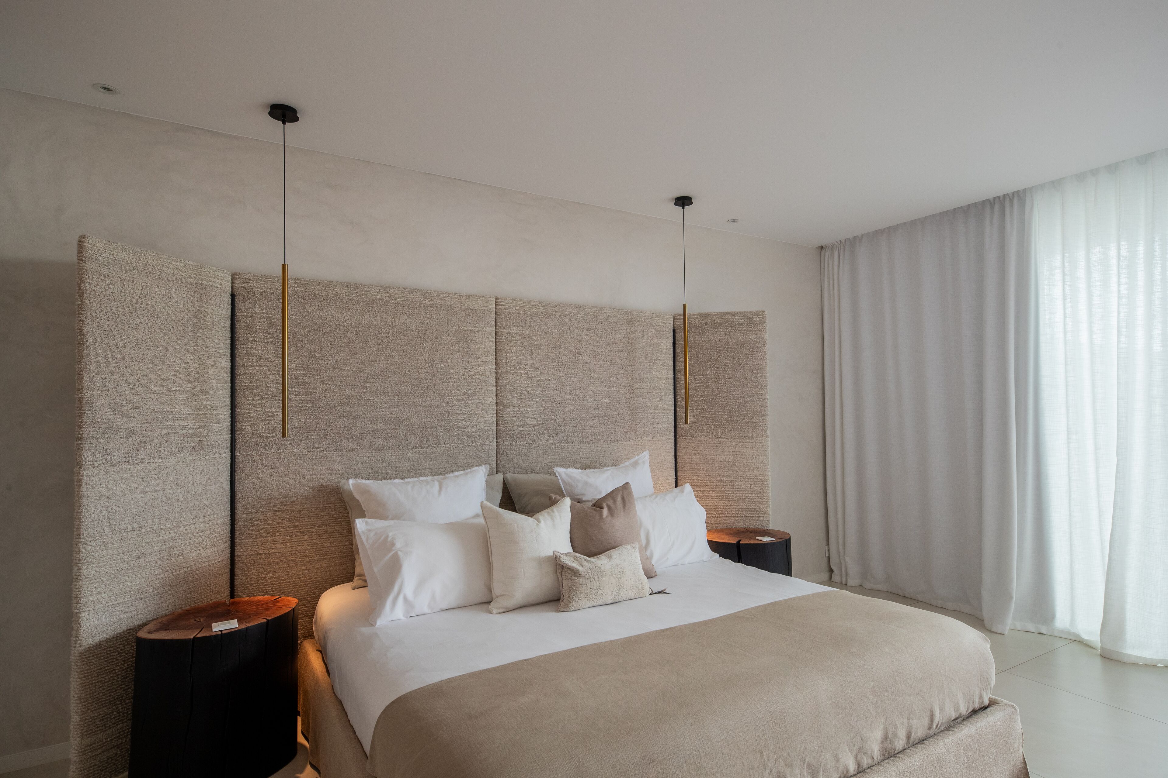 Ein modernes Schlafzimmer mit einem großen Bett, vielen Kissen, einem Nachttisch und einer Pendelleuchte.