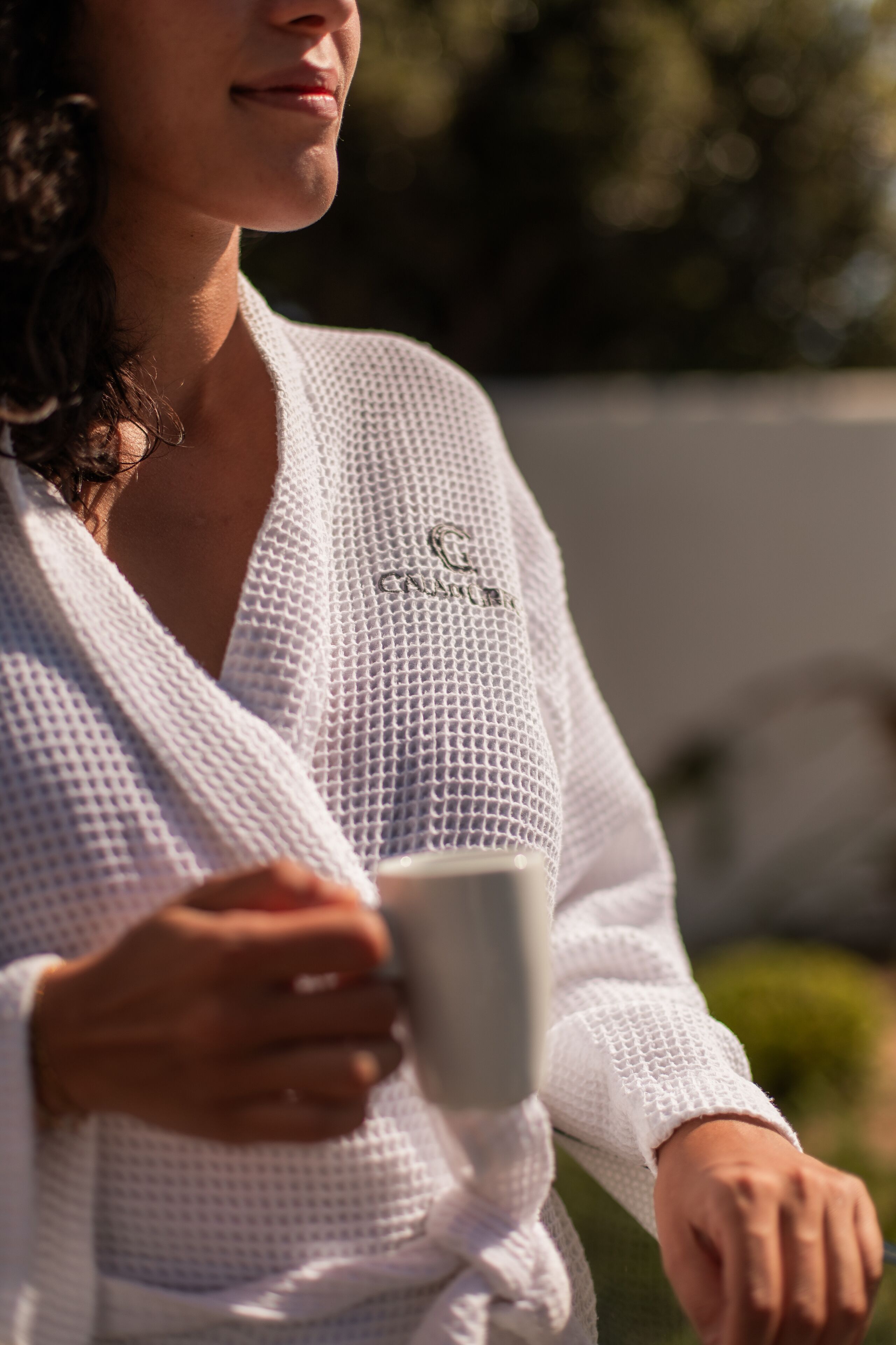 A person in a white robe holding a cup, with a blurred outdoor background.